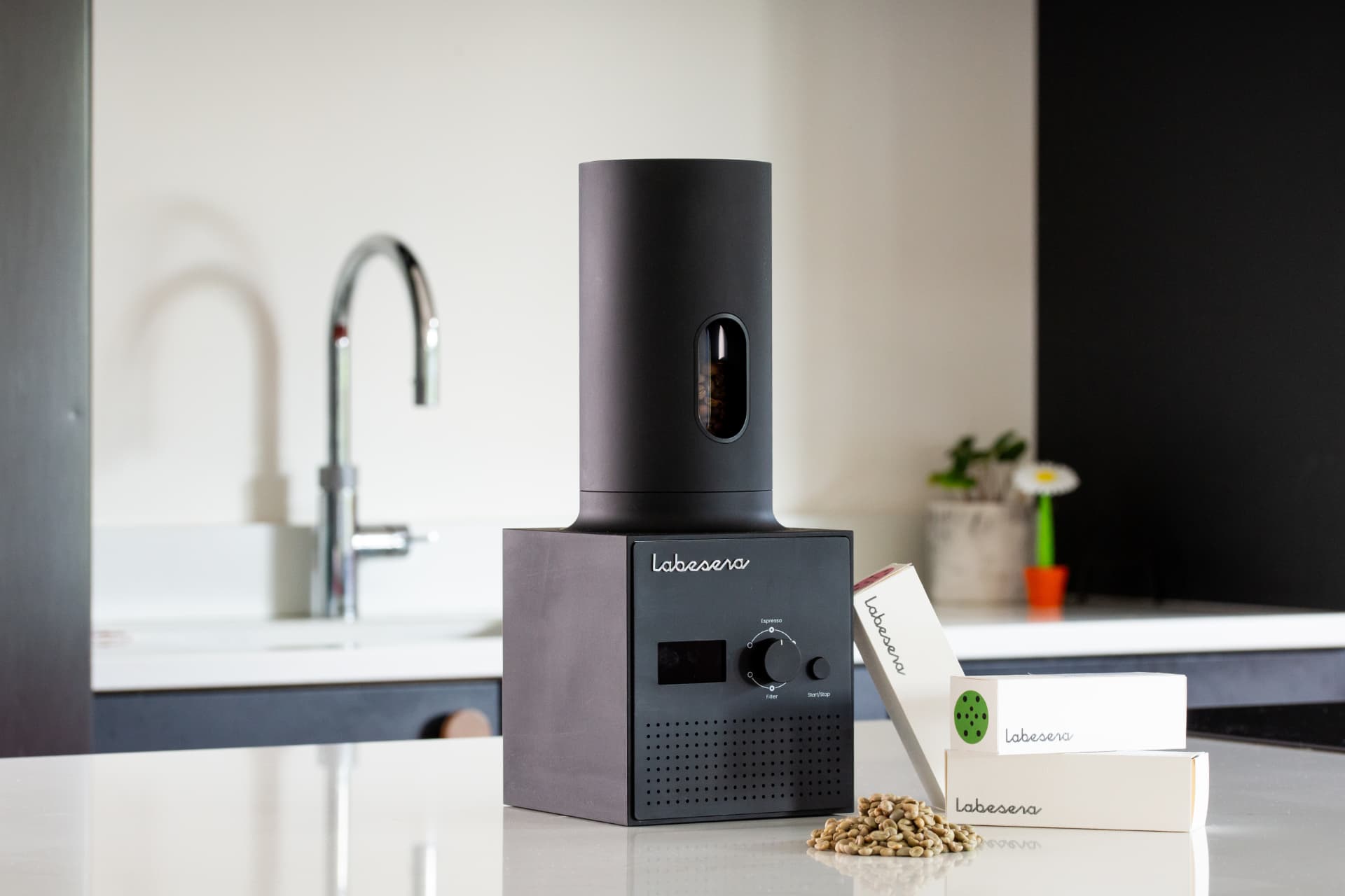 Labesera home coffee roaster on a kitchen counter beside three packs of green coffee